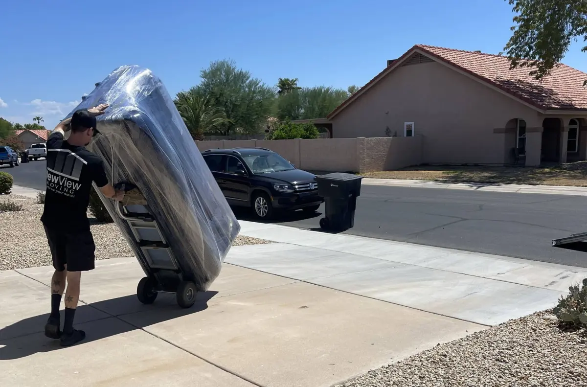 A NewView mover rolls a shrink-wrapped load on a dolly past a parked truck