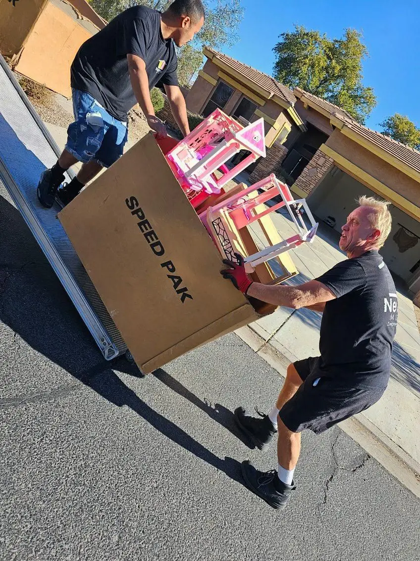 Two NewView movers guide a large box down the truck ramp