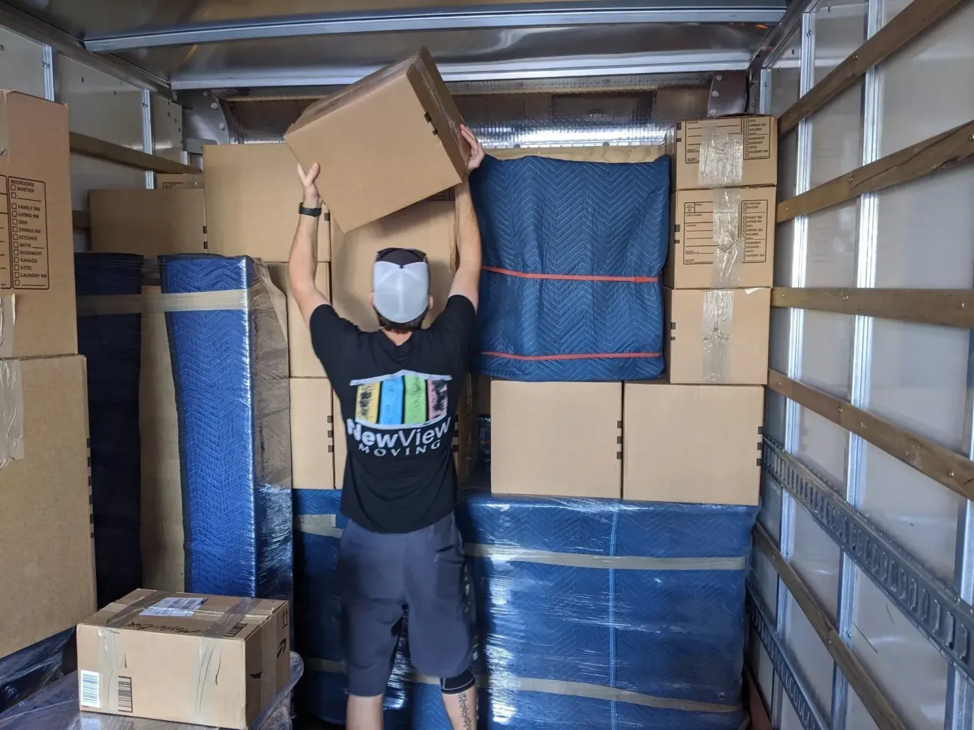 A mover stacks boxes inside the truck between padded furniture