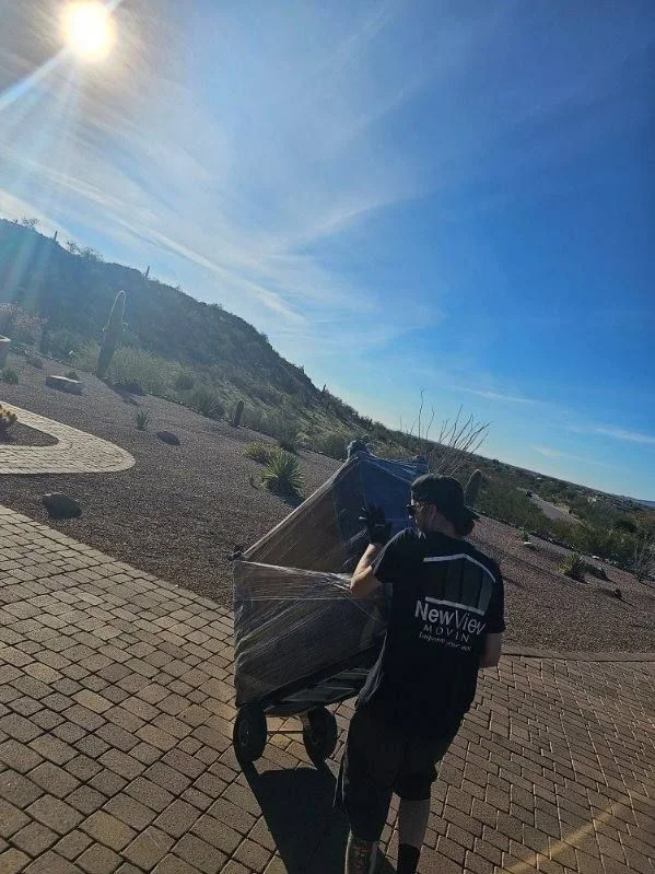 A NewView mover in the company shirt wheels a shrink-wrapped load across a sunny desert hillside